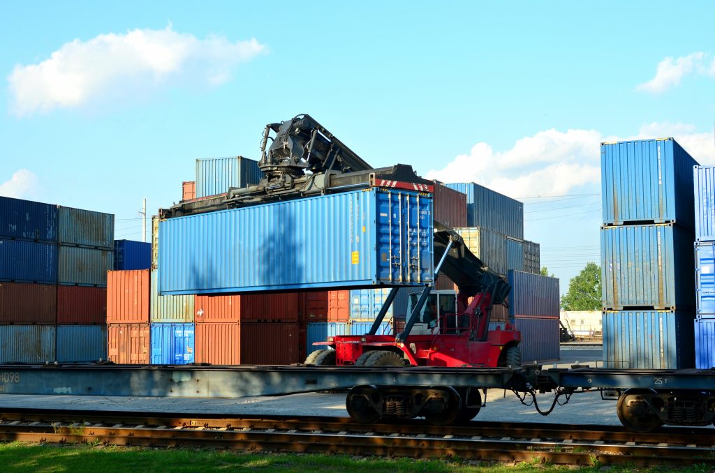 Shipping container loading by richtracker on the freight rail car at logistic warehouse port. Ocean Freight Cargo Shipping, Intermodal Container Freight concept - Image