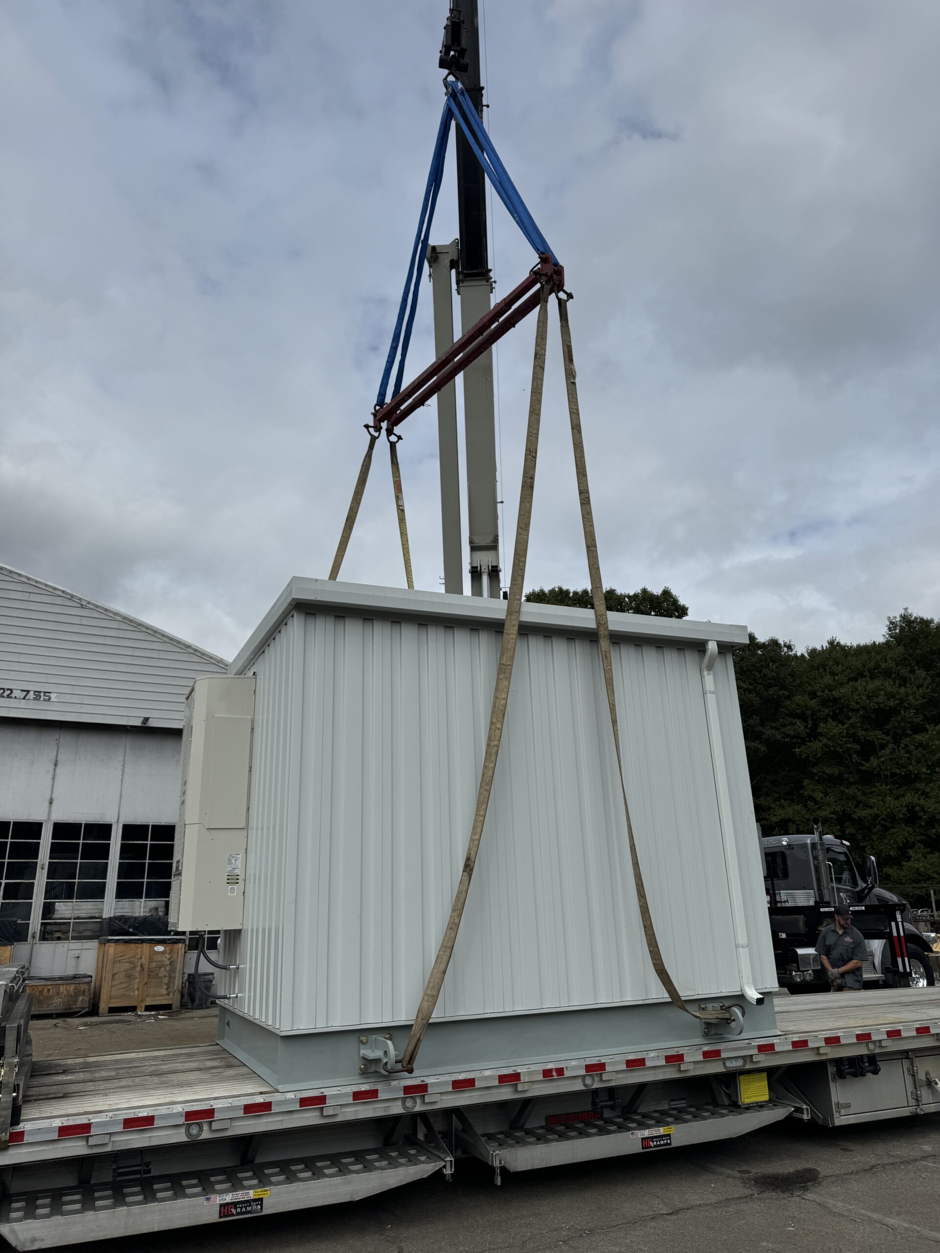 Crane lifting UPS enclosure onto flatbed for secure transport
