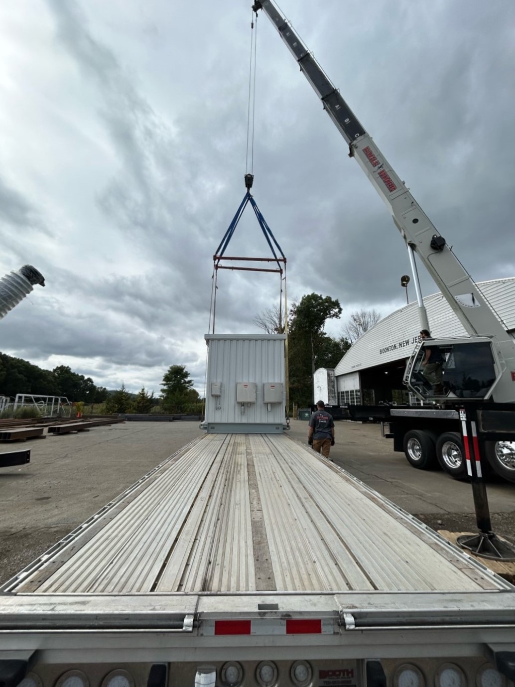 Rear view of crane lowering UPS enclosure onto flatbed trailer